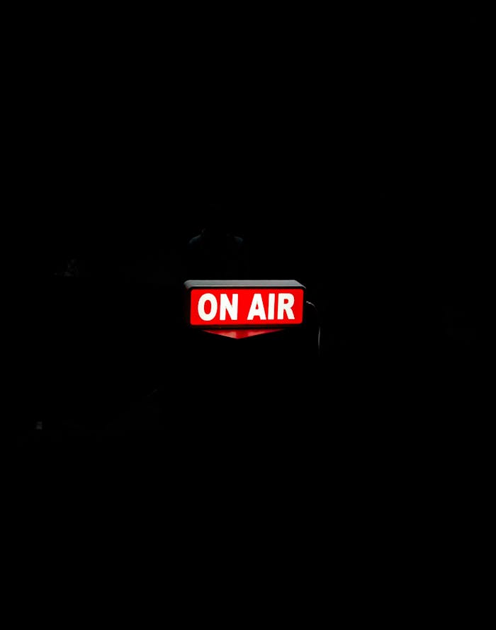 Bright 'On Air' sign glows in dark studio, creating moody atmosphere.
